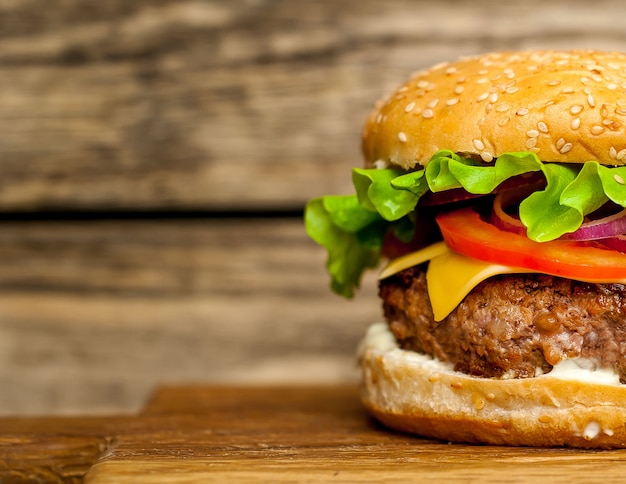 Hausgemachter Hamburger mit Salat, Tomate, Käse und Gurke auf einem Schneidebrett