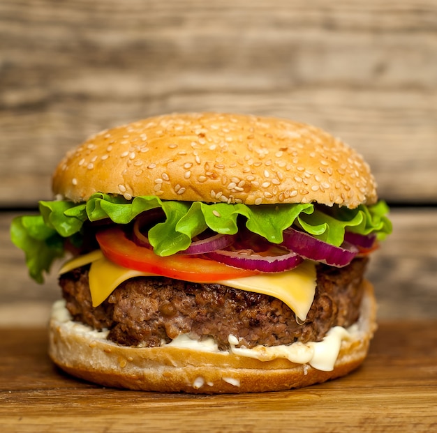 Hausgemachter Hamburger mit Salat, Tomate, Käse und Gurke auf einem Schneidebrett