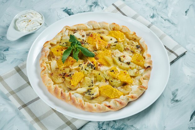 Hausgemachter heißer Obstkuchen mit Orange, Äpfeln, Birnen und Banane mit Sahne. Essen im Dessert