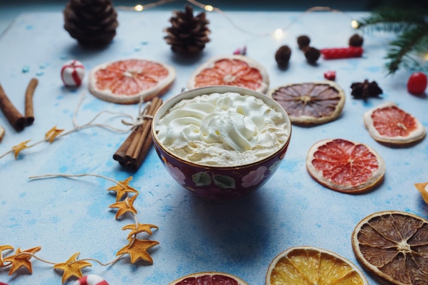 Hausgemachter Kakao oder heiße Schokolade mit cremefarbenen, getrockneten Orangen, Tannenbaum-Zimtbonbons auf blauem Betonhintergrund. Weihnachten oder Neujahr trinken gemütliche Heimdekoration mit selektivem Fokus