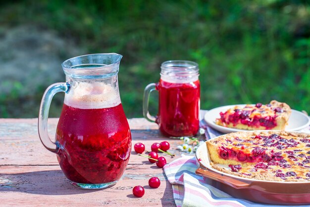 Hausgemachter Kirschkuchen und rotes Kirschgetränk auf dem Holztisch im Gartenhintergrund, Nahaufnahme