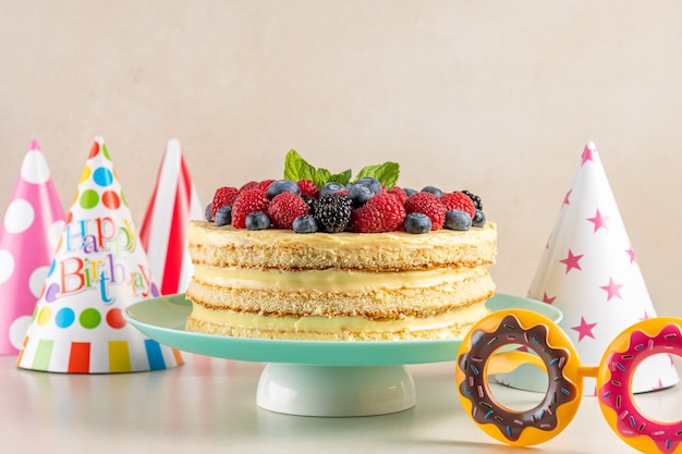 Hausgemachter Kuchen mit frischen Beeren und Geburtstagshut auf heller Oberfläche.