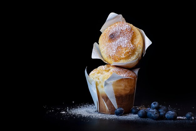 Hausgemachter Kuchen. Muffins mit Puderzucker und Blaubeeren auf einem schwarzen Hintergrund