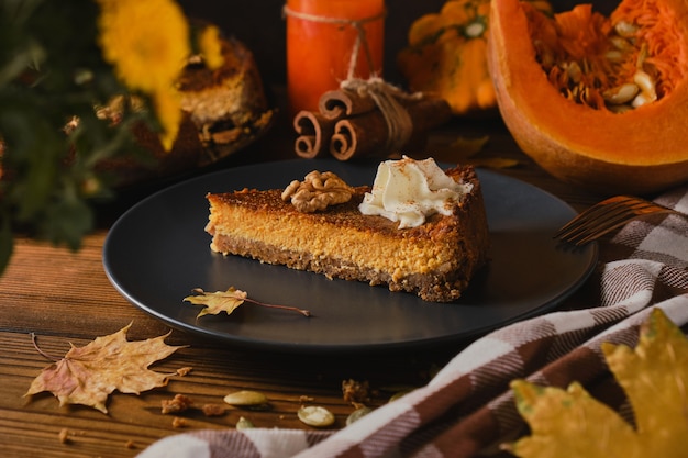 Hausgemachter Kürbis-Käsekuchen mit Schlagsahne auf schwarzem Teller für Thanksgiving. Das Tonen. selektiver Fokus