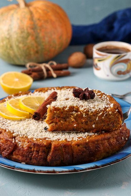 Hausgemachter Kürbiskuchen mit Zitrone, Zimt und Walnüssen, mit Kokosnuss bestreut, in Scheiben geschnitten, auf einer hellblauen Oberfläche mit einer Tasse Kaffee