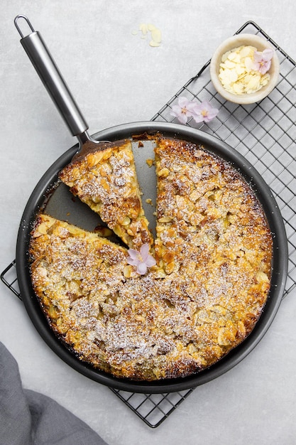 Hausgemachter Mandelkuchen mit geschnittener Mandelkruste und Puderzucker auf hellgrauem Betonhintergrund. Ansicht von oben.