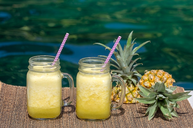 Hausgemachter Mango-Ananas-Smoothie mit Kokosmilch in zwei Glasbechern in der Nähe des Pools