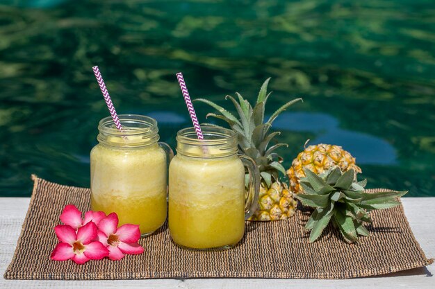 Hausgemachter Mango- und Ananas-Smoothie mit Kokosmilch in zwei Glasbechern in der Nähe des Swimmingpools Insel Bali Indonesien Erfrischendes tropisches Fruchtgetränk