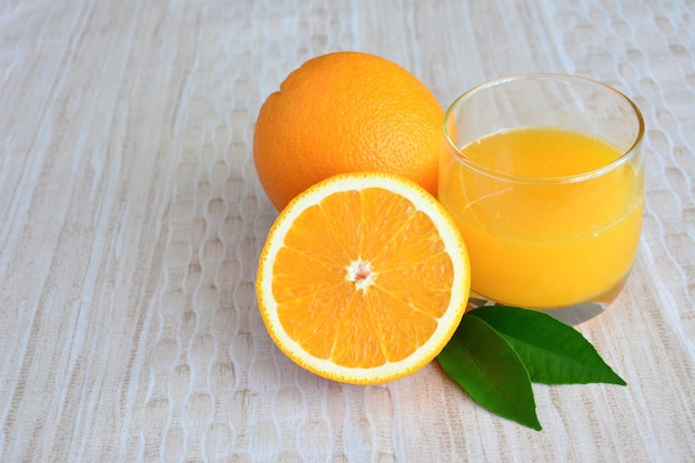 hausgemachter Orangensaft im Trinkglas mit Orangen und grünem Blatt auf pastellfarbenem Hintergrund