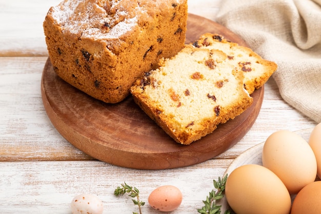 Hausgemachter Osterkuchen mit Rosinen und Eiern auf Teller auf weißem Holzhintergrund, Seitenansicht aus nächster Nähe