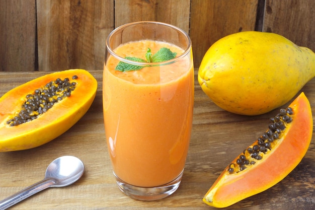 Hausgemachter Papaya-Smoothie mit tropischen Früchten und Minze in Glasschale über rustikalem Holztisch. Ansicht von oben