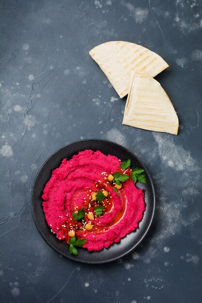 Hausgemachter Rote-Bete-Hummus in schwarzer Keramikschale auf altem dunklem Betonhintergrund. Selektiver Fokus. Ansicht von oben.