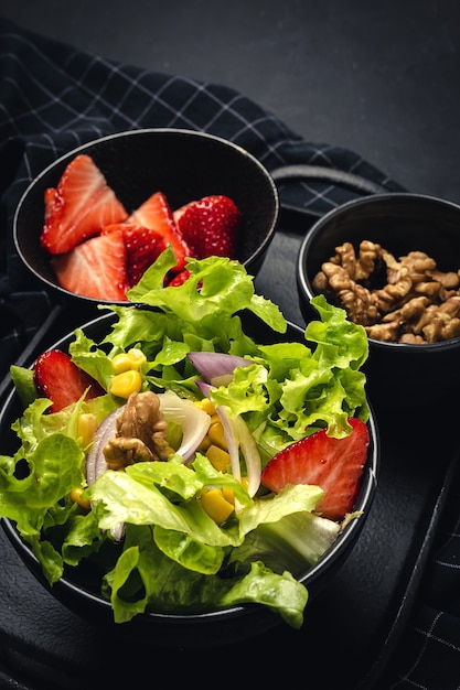 Hausgemachter Salat mit Salat, Erdbeeren, roten Zwiebeln, Mais; Olivenöl und Walnüsse in einer Schüssel. Veganes Lebensmittelkonzept