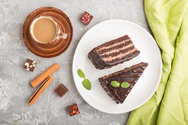 Hausgemachter Schokoladenkuchen mit Milchcreme und einer Tasse Kaffee auf einer grauen Betonoberfläche. Draufsicht, Nahaufnahme.