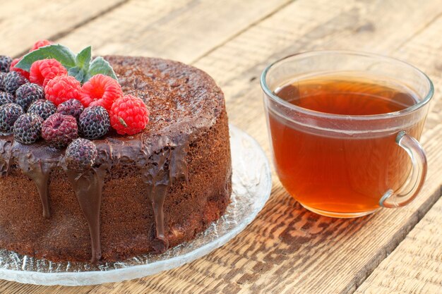 Hausgemachter Schokoladenkuchen mit Minzblättern und Himbeeren auf Teller mit Tasse Tee