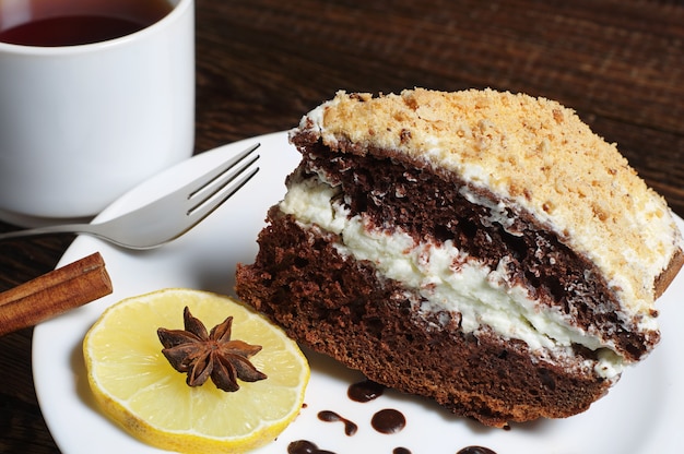 Hausgemachter Schokoladenkuchen mit Schlagsahne und Tasse Tee auf dunklem Holztisch