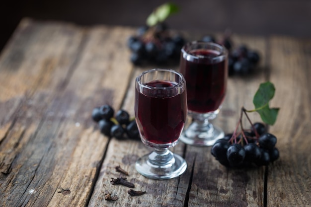 Hausgemachter schwarzer Apfelbeerwein oder Likör mit reifen Beeren auf Holzuntergrund