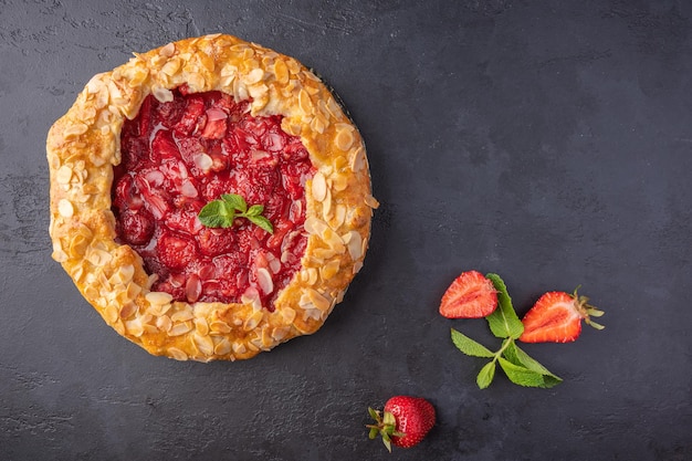 Hausgemachter Sommerkuchen mit Erdbeerminze und Mandelblüten auf dunklem Hintergrund mit Draufsicht