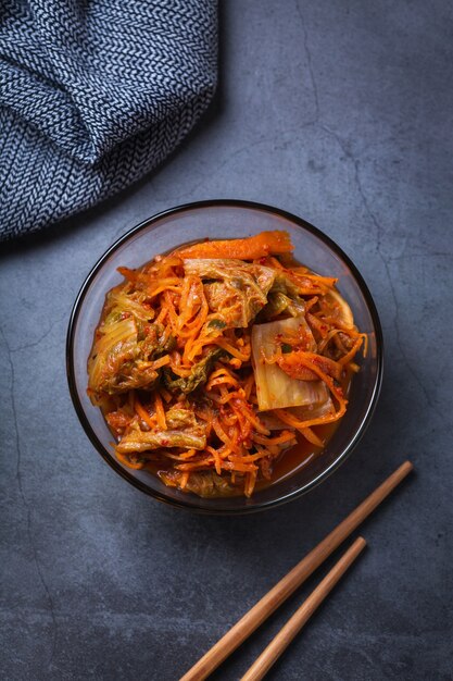 Hausgemachter traditioneller koreanischer Kimchi-Kohlsalat aus biologischem Anbau mit Stäbchen auf einem dunklen Tisch. Fermentiertes vegetarisches, vegan konserviertes Darmgesundheits-Lebensmittelkonzept