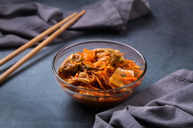 Hausgemachter traditioneller koreanischer Kimchi-Kohlsalat aus biologischem Anbau mit Stäbchen auf einem dunklen Tisch. Fermentiertes vegetarisches, vegan konserviertes Darmgesundheits-Lebensmittelkonzept