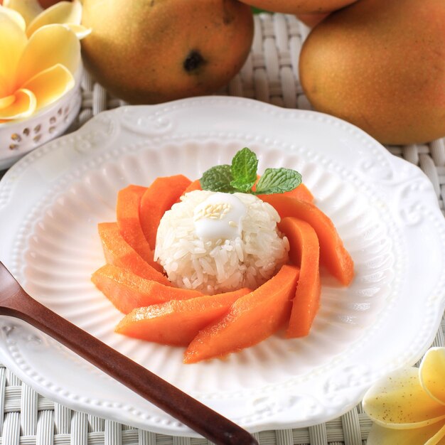 Hausgemachter tropischer thailändischer Dessert-Mango-Klebreis auf weißem Teller, serviert mit köstlicher Vanille-Kokosmilch und Sprean mit Sesam