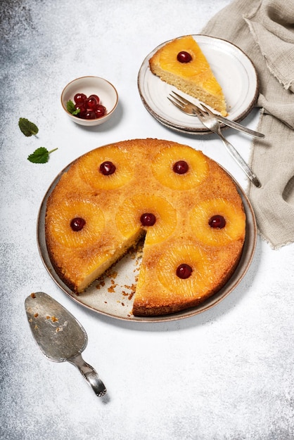 Hausgemachter umgedrehter Ananaskuchen mit kandierten Kirschen und einem abgeschnittenen Stück auf einem Teller