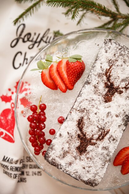 Hausgemachter Weihnachtsschokoladenkuchen mit Puderzucker bestreut mit roten Johannisbeeren und Erdbeeren