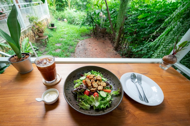 Hausgemachter Wurstsalat mit frischem Gemüse, Tometo und einem Glas Americano-Kaffee auf Holztisch