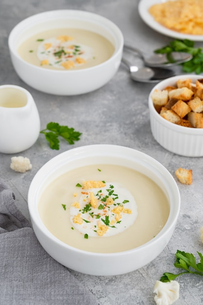 Hausgemachtes Blumenkohlsuppenpüree in einer weißen Schüssel mit Käse-Sahne-Gewürzen und frischer Petersilie