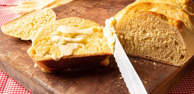 Hausgemachtes Brot, geschnittenes hausgemachtes Brot mit Butter auf Holz und eine rot-weiß karierte Tischdecke, ein Messer und ein Bündel Weizen.