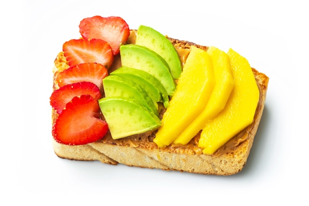 Hausgemachtes Brot mit Erdnussbutter bedeckt, oben mit Erdbeeren, Mango und Avocado auf weißem Teller. Gesundes Essen zum Abnehmen. Gesundes Frühstückskonzept.