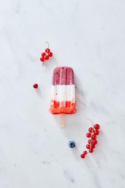 Hausgemachtes dreifarbiges Beeren-Eis am Stiel mit Eis und Beeren auf Marmorhintergrund. Sommer-Food-Konzept, Draufsicht. Kopieren Sie Platz für Text.