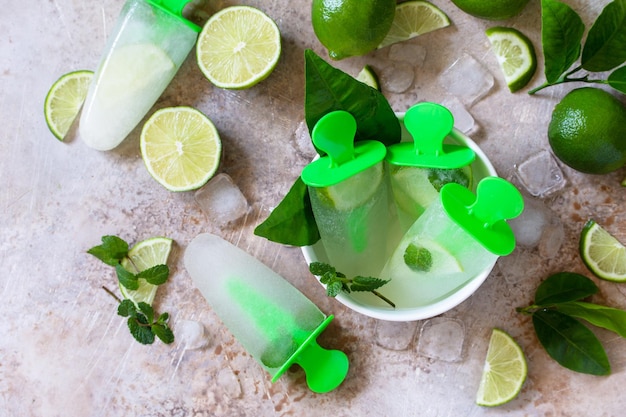 Hausgemachtes Eis am Stiel mit Limettensaft und Minz-Mojito-Fruchteis auf einem hellen Stein Draufsicht