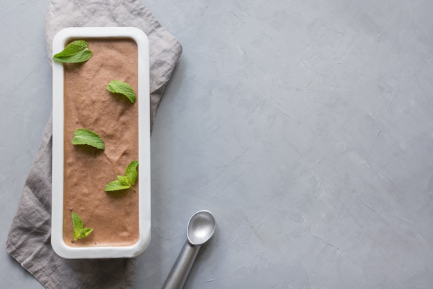 Hausgemachtes Eis der Bananenschokolade mit Minze im Behälter auf grau.