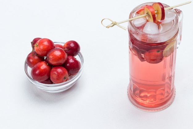 Hausgemachtes erfrischendes Sommerapfelgetränk mit Eis im Glas. Geschnittene Äpfel am Stiel. Kleine rote Äpfel in Glasschale. Weißer Hintergrund. Draufsicht.