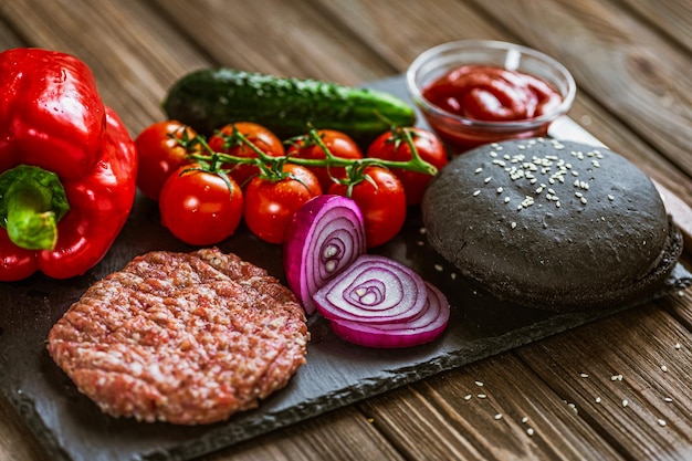 Hausgemachtes Essen Vorderansicht der Zutaten für schwarzen Rindfleischburger auf schwarzem Steinbrett Leckeres Essen