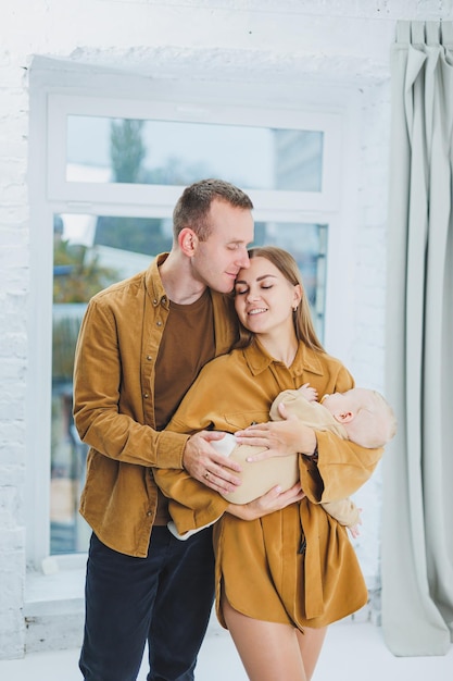 Hausgemachtes Familienfoto auf weißem Hintergrund glücklicher Eltern mit einem neugeborenen Baby, das in ihren Armen schläft Eine glückliche Mutter und ein glücklicher Vater halten ihren viermonatigen Sohn in den Armen