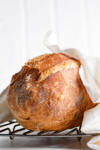 Hausgemachtes frisch gebackenes Brot auf einem Holzbrett und hellgrauem Marmortisch verziertes Textilhandtuch.