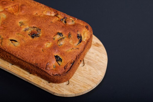 Hausgemachtes Fruchtkuchenlaib des Lebensmittels auf hölzernem Brett mit schwarzem Hintergrund