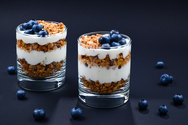 Hausgemachtes gebackenes Müsli mit Joghurt und Blaubeeren in einem Glas auf Schwarz