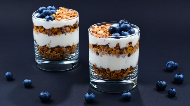 Hausgemachtes gebackenes Müsli mit Joghurt und Blaubeeren in einem Glas auf Schwarz