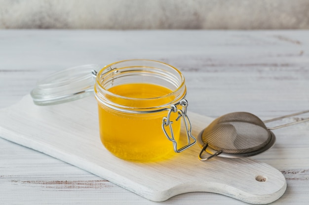 Hausgemachtes Ghee oder geklärte Butter in einem Glas auf weißem Holztisch.