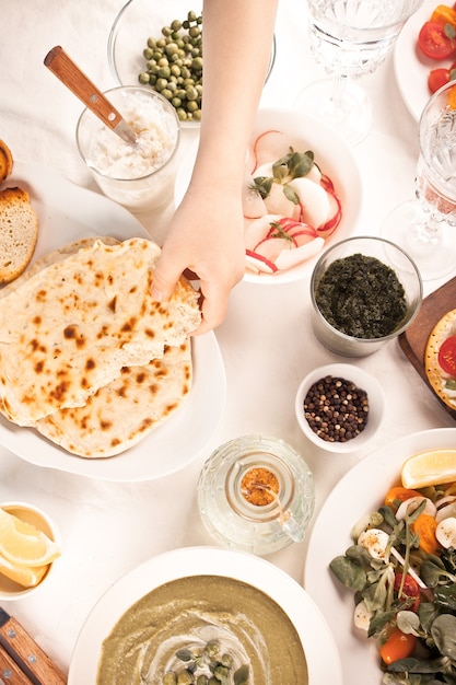 Hausgemachtes indisches Naan-Fladenbrot mit frischem Salat und Dips auf dem Esstisch. Kinderhand verteilt den Dip auf einem Stück Fladenbrot.