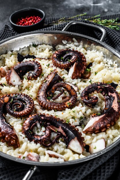 Hausgemachtes italienisches Risotto mit Tintenfisch in einer Pfanne. Schwarzer Hintergrund. Draufsicht