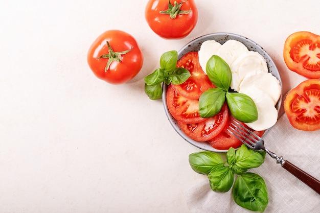 Hausgemachtes Konzept für gesunde Mahlzeiten: Kirschtomaten, Mozzarella-Bällchen, Gewürze, Olivenöl und frisches Basilikum. Mozzarella-Salat über weißer Texturoberfläche. Draufsicht, flach liegen