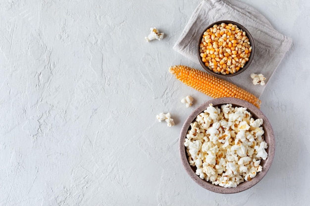 Hausgemachtes leckeres traditionelles Popcorn, rohe Maissamen und Maiskolben auf Betonhintergrund Die Draufsicht mit Kopierraum