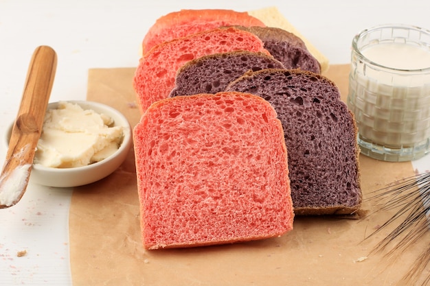 Hausgemachtes lila und rosa Brot aus japanischer lila Süßkartoffel. mit natürlicher Farbe. Serviert auf Backpapier weißer Hintergrund mit Milch und Yam in Scheiben geschnitten. Konzept für gesunde Ernährung Bäckerei