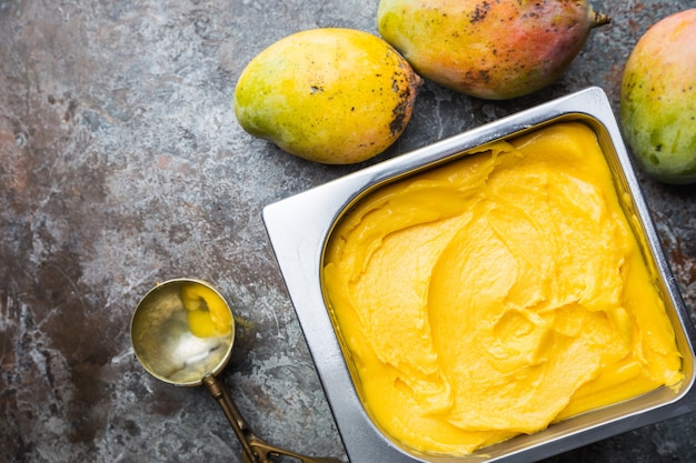 Hausgemachtes Mango-Eis in Schalen mit frischen Früchten über Dunkelgrau