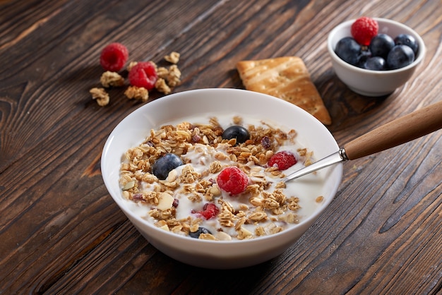 Hausgemachtes Müsli-Müsli-Frühstück mit Naturjoghurt, Blaubeeren und Himbeeren auf rustikalem Holztisch