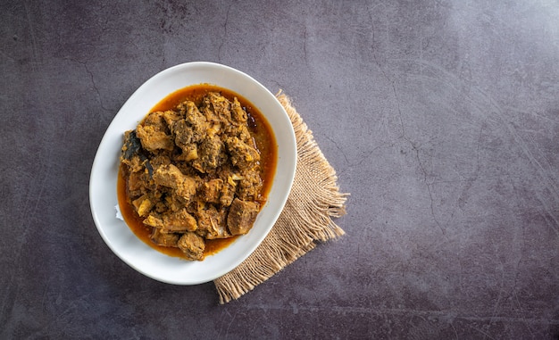 hausgemachtes Rindfleisch-Curry in weißer Schüssel mit Vintage-Tischdecke auf dunkler Schieferfliese-Draufsicht